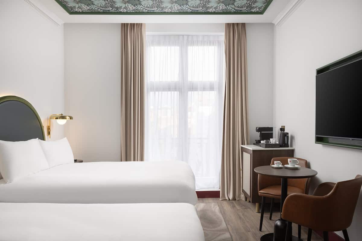 A hotel room with a bed, a desk with a coffee maker, and a TV on the wall.