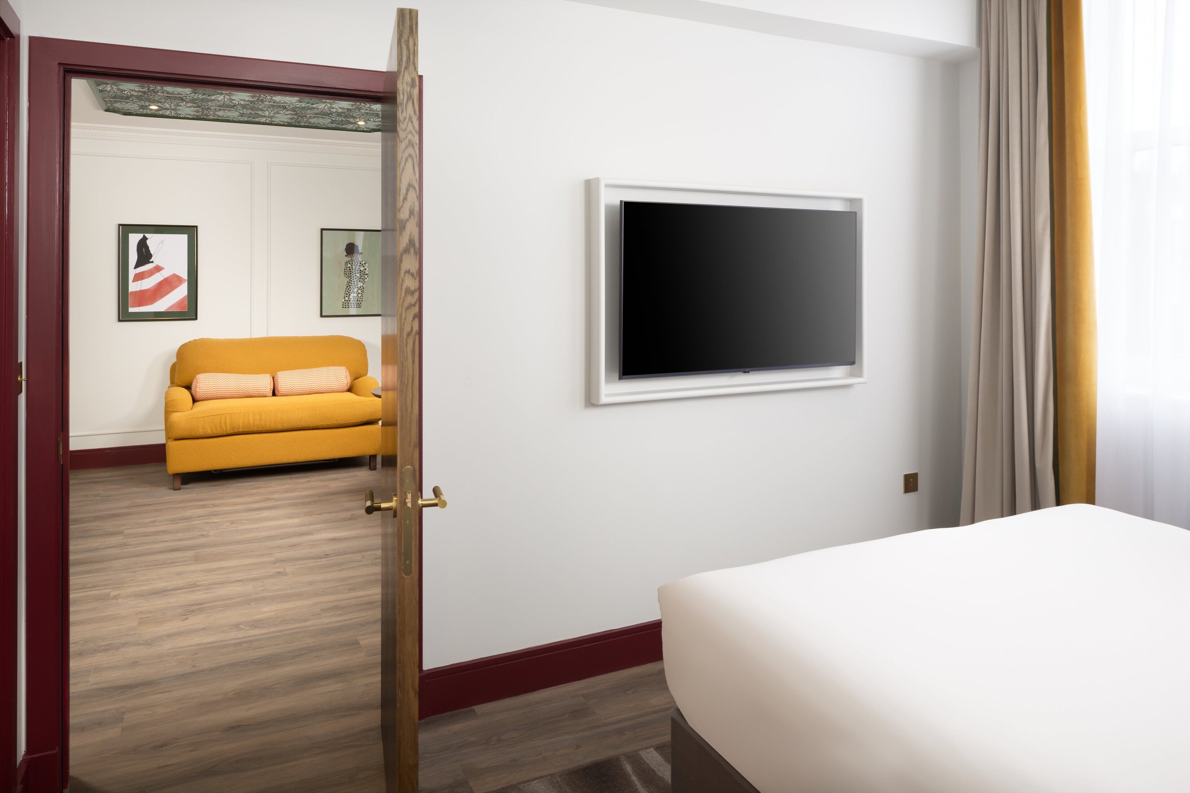 A hotel room with a bed, a yellow sofa, a flat-screen TV, and two framed pictures on the wall.