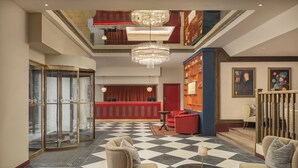 Eine Lobby mit Schachbrettmuster-Boden, einer Glaselevator und einem roten Empfangsschalter.