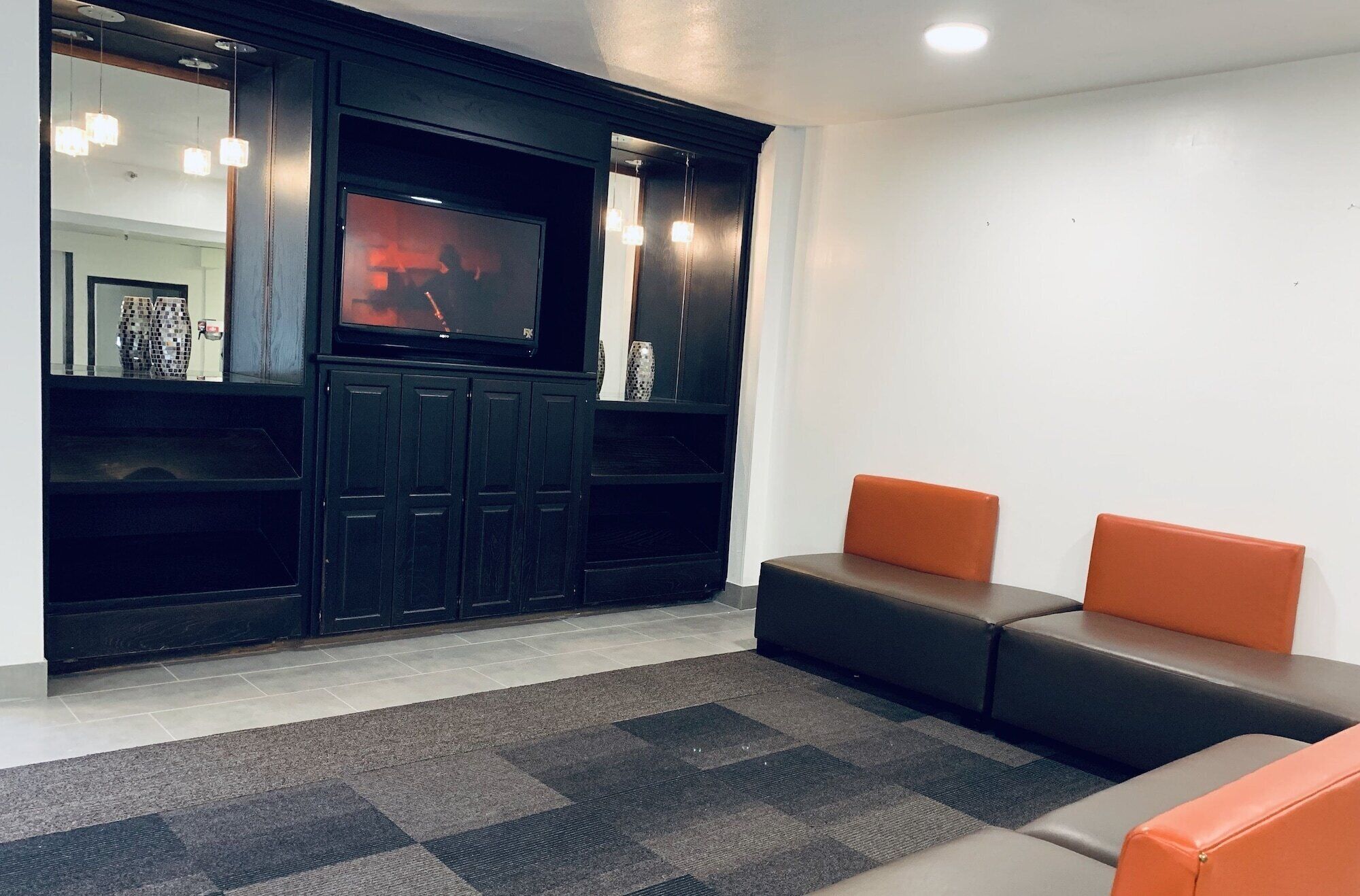Een moderne wachtruimte met een flatscreen televisie, donkere houten kasten en oranje zitplaatsen.