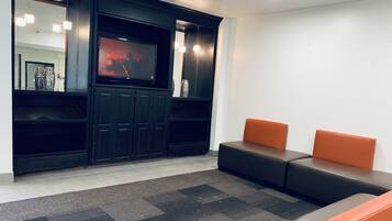 A modern waiting area with a flat-screen TV, dark wooden cabinets, and orange seating.