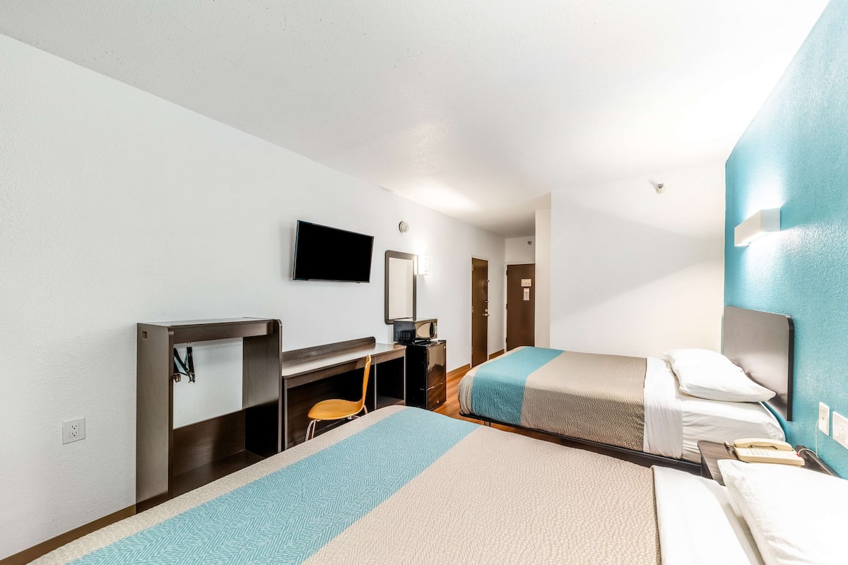 Ein Hotelzimmer mit zwei Betten, einem Schreibtisch, einem Stuhl, einem Fernseher und einer Badezimmertür.