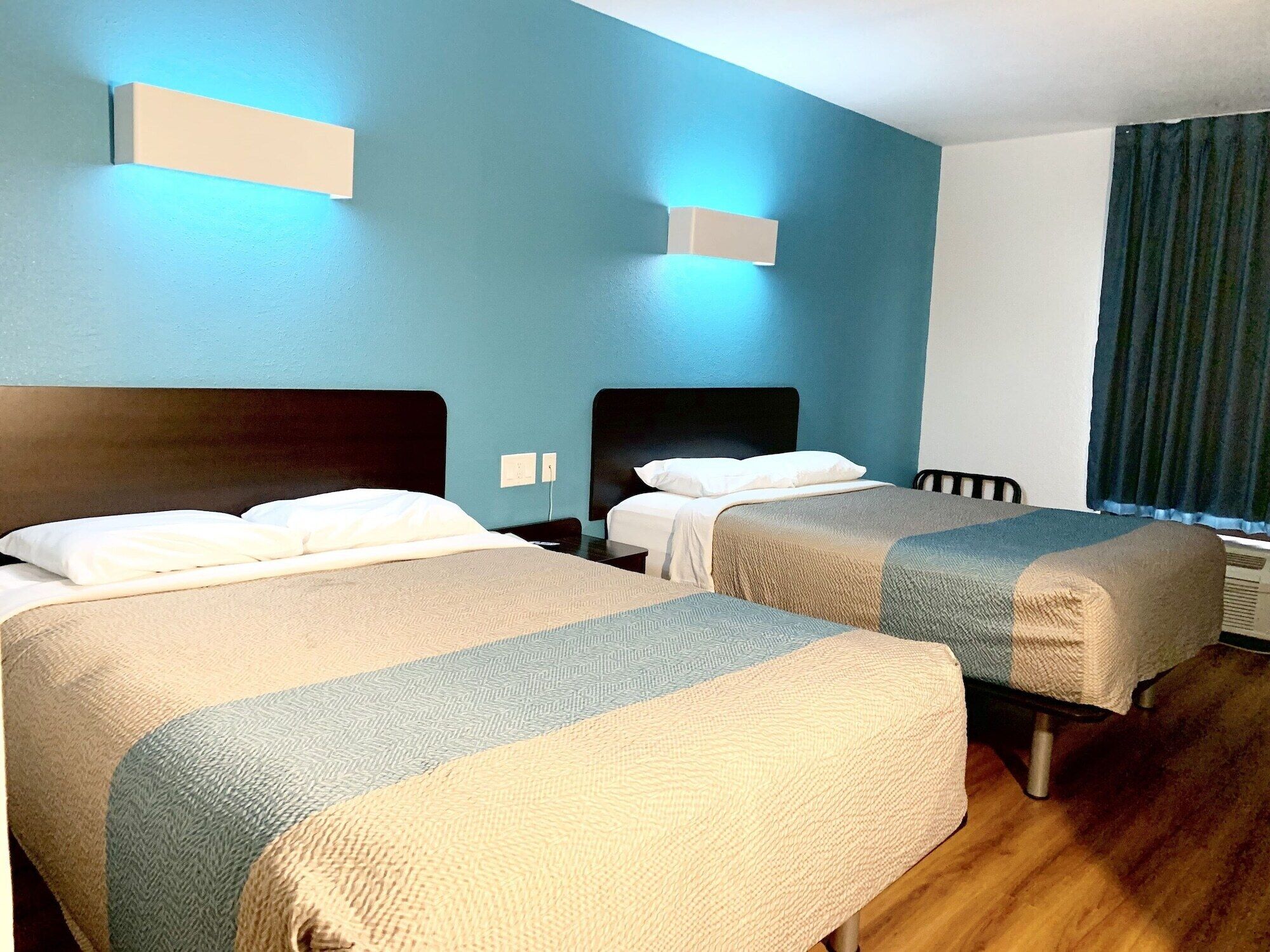 Habitación de hotel con dos camas, piso de madera y una ventana con cortinas.