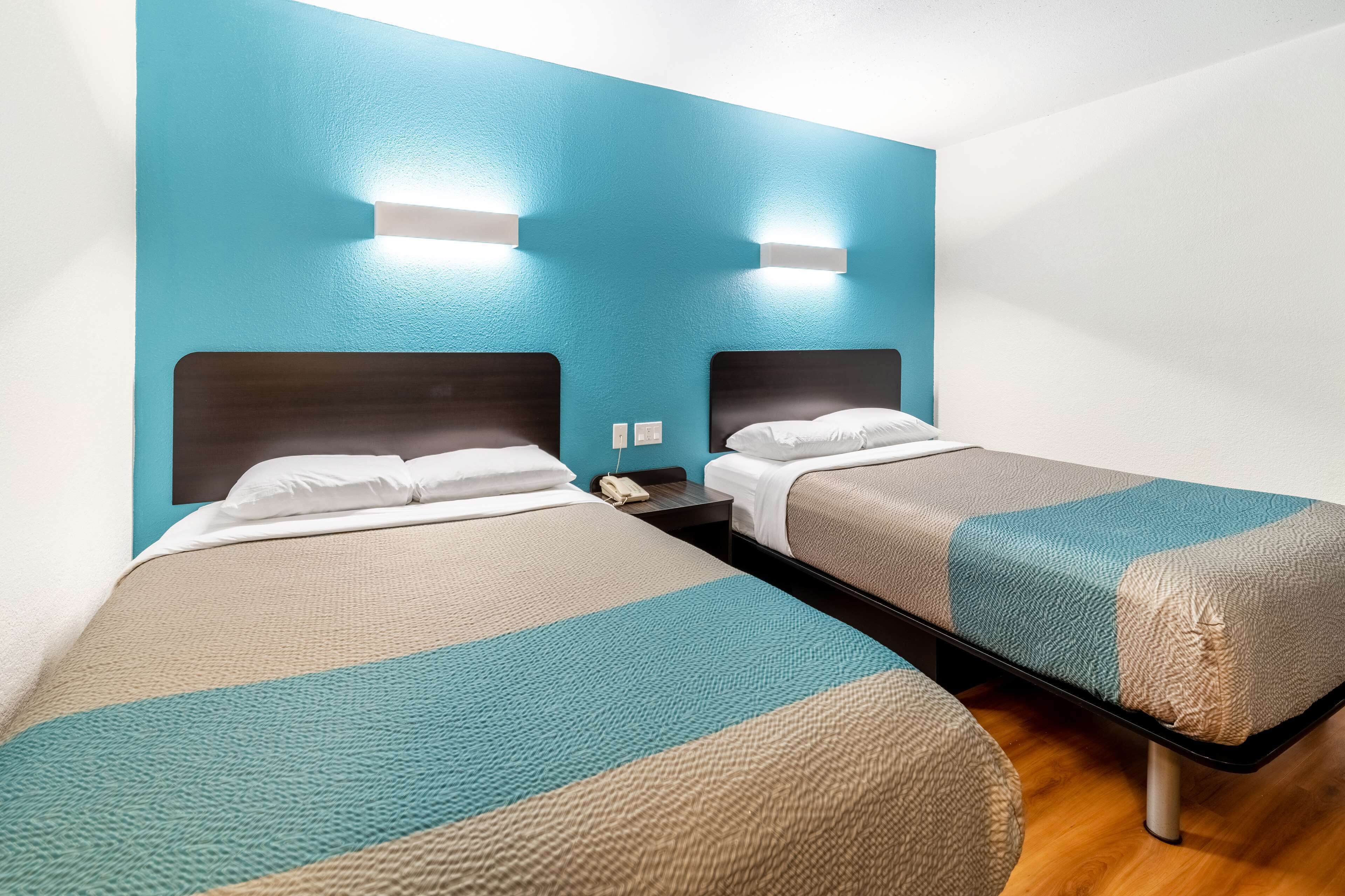 Habitación de hotel con dos camas individuales, piso de madera y una pared de acento color verde azulado.