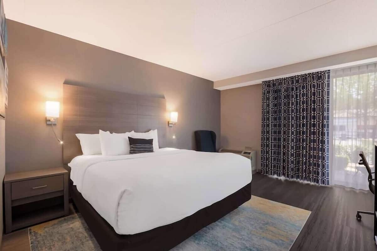 A modern hotel room with a large bed, bedside tables, a desk, and a patterned curtain.