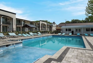 A swimming pool with lounge chairs, a fenced area, and a building with balconies.