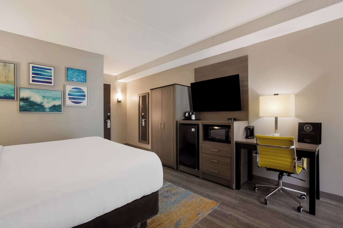A hotel room with a bed, a desk with a chair, a flat-screen TV, a coffee maker, and artwork on the wall.