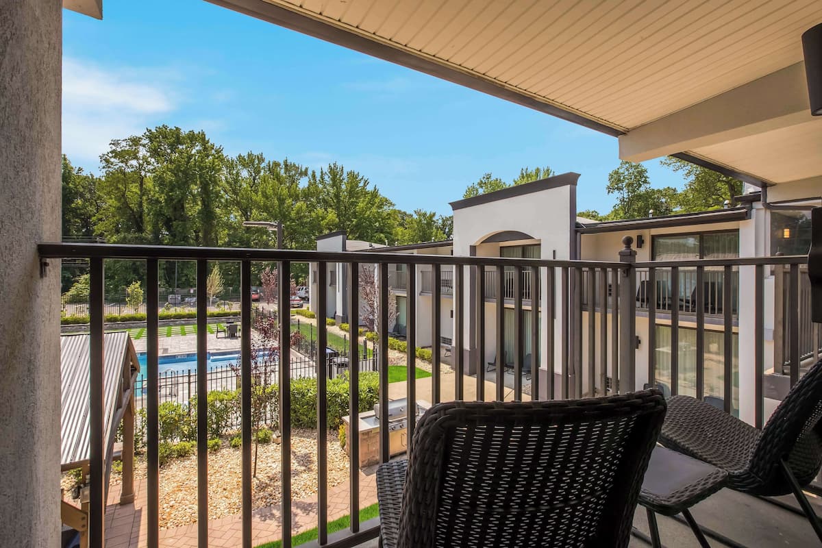 A balcony with wicker chairs, a pool, and a view of a residential area.