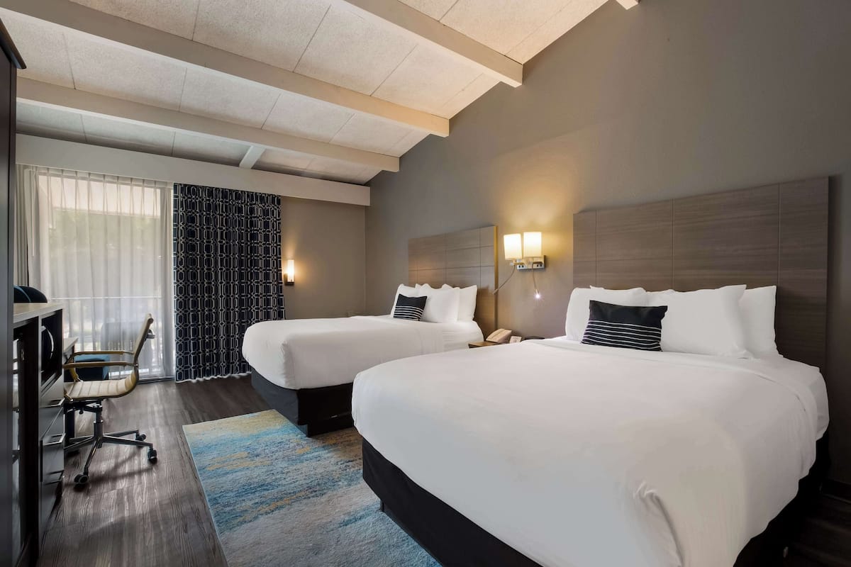 A hotel room with two beds, a desk, and a chair.