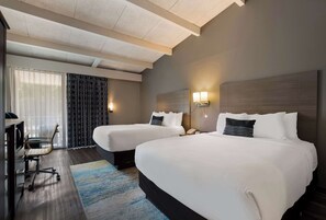 A hotel room with two beds, a desk, and a chair.