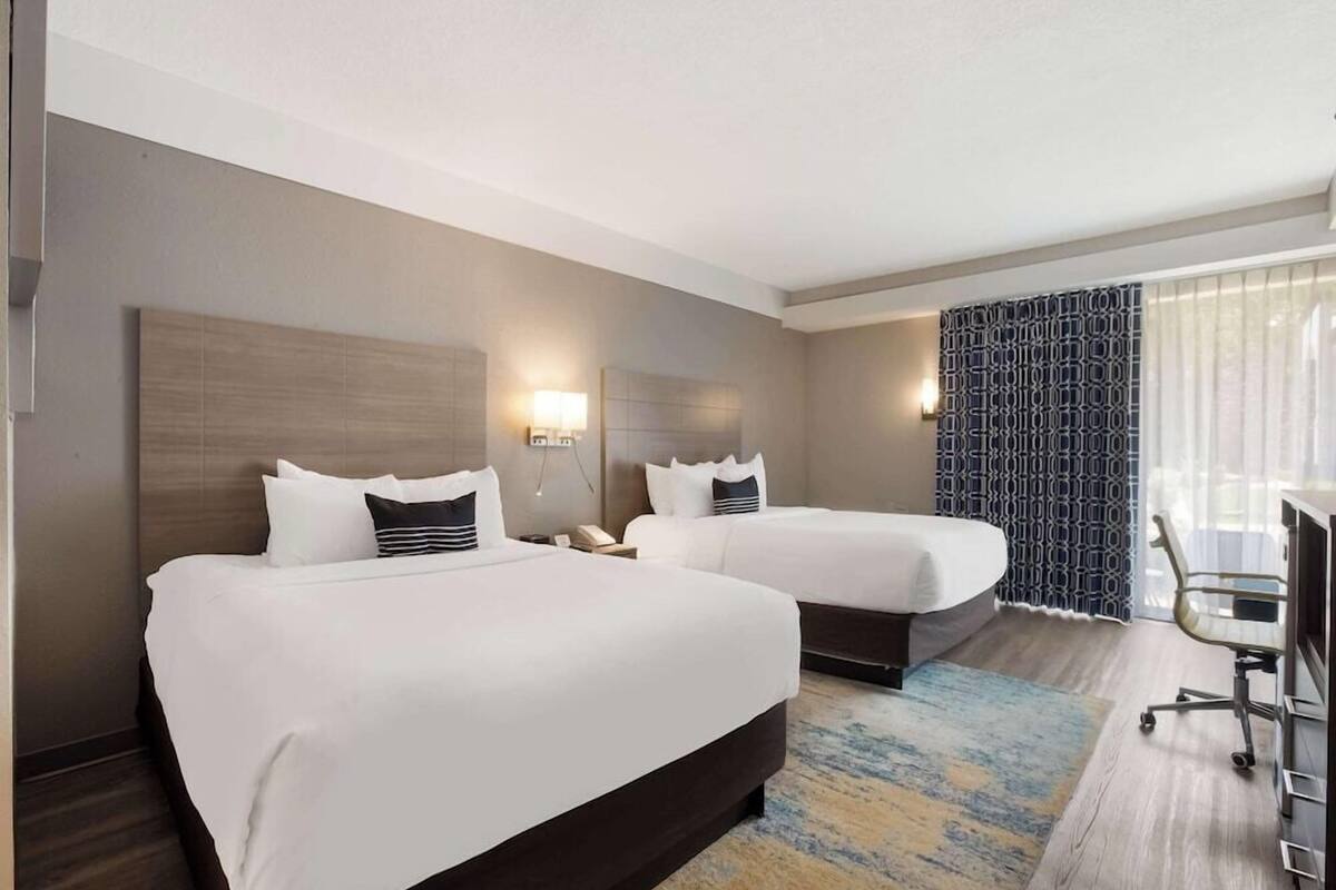 A hotel room with two beds, a desk, a chair, and a patterned curtain.