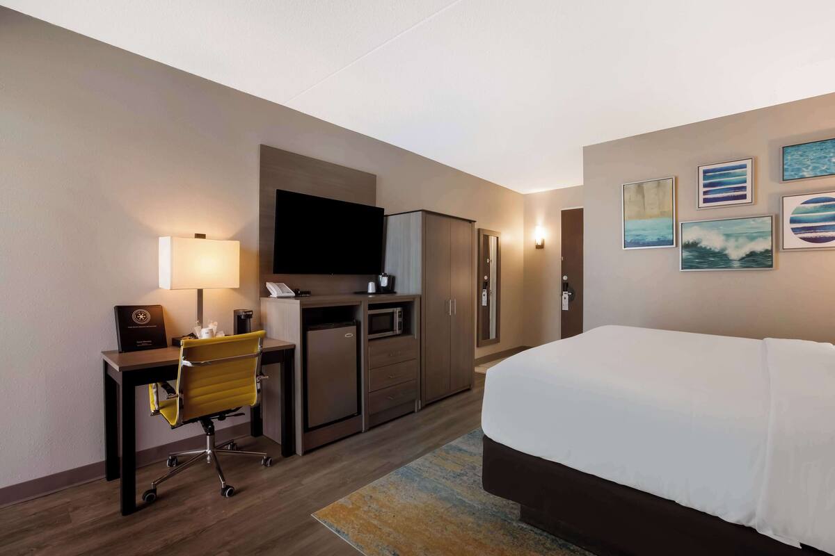 A hotel room with a bed, desk, chair, television, wardrobe, and artwork on the wall.