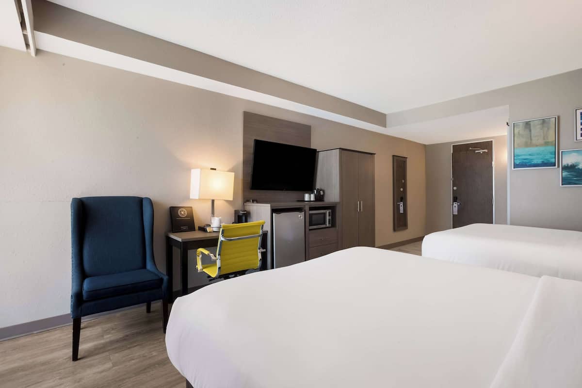A hotel room with two beds, a desk with a lamp, a television, a microwave, and a small kitchenette.