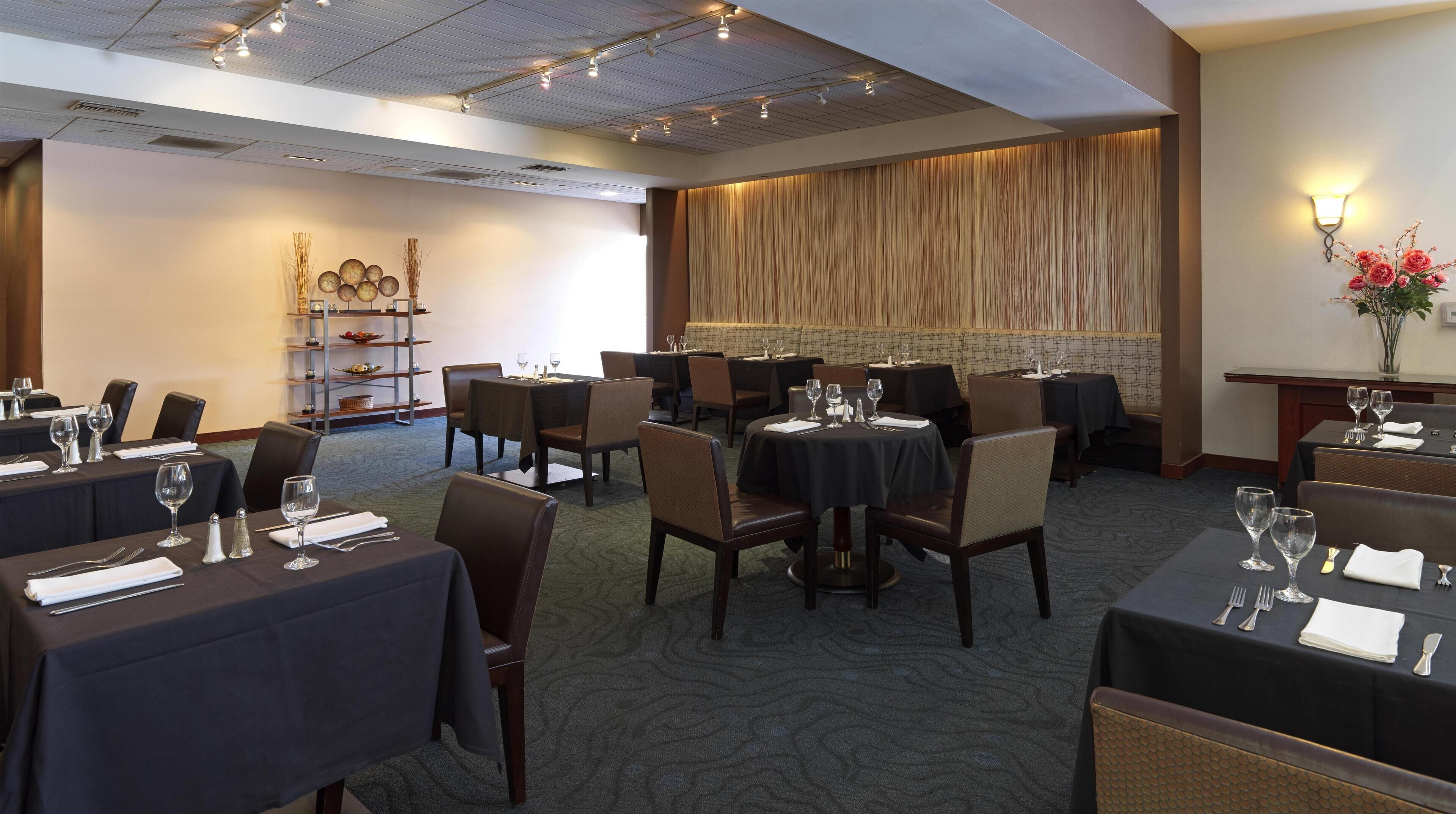 A hotel dining area with tables set for guests, a decorative wall, and a ceiling with recessed lighting.