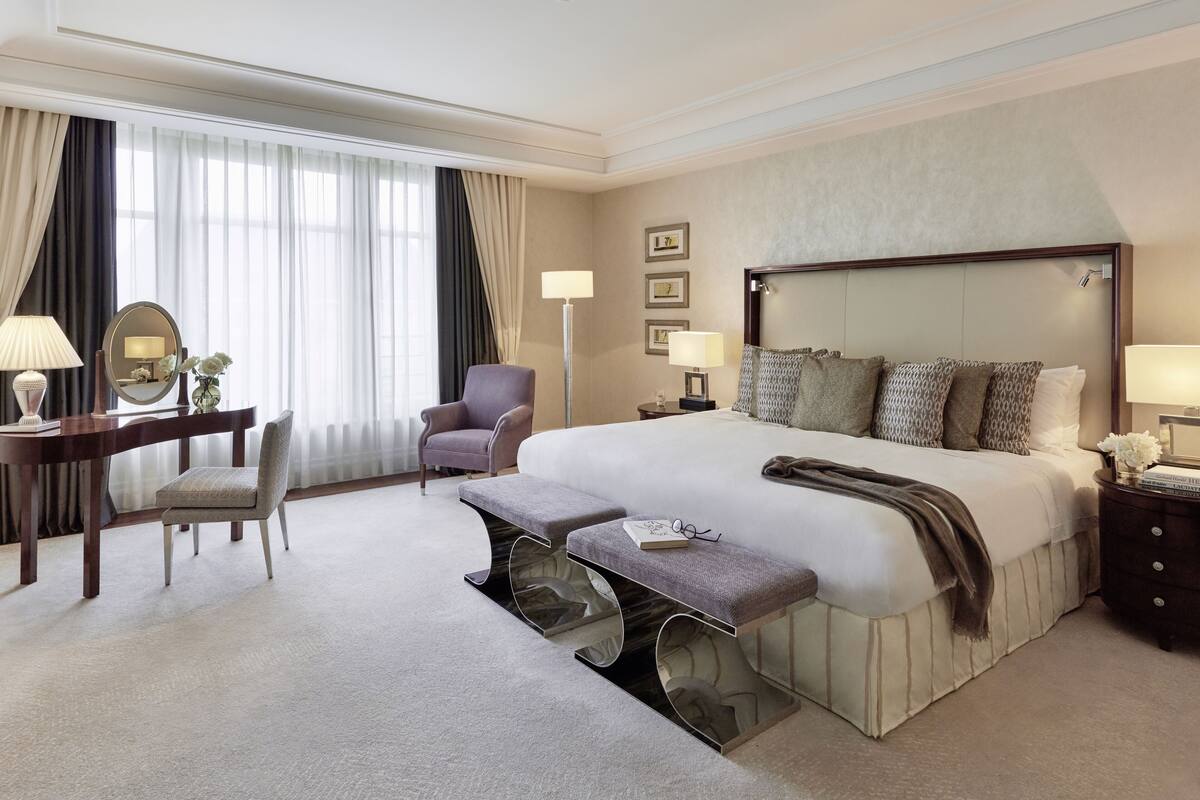 Habitación de hotel con una cama grande, un escritorio con silla, un banco y una mesita de noche con lámparas.