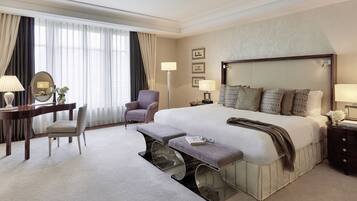 Habitación de hotel con una cama grande, un escritorio con silla, un banco y una mesita de noche con lámparas.