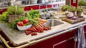 Una encimera de cocina con verduras frescas, un fregadero y diversos utensilios de cocina.
