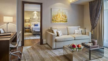 Ein modernes Hotelzimmer mit einer Couch, einem Couchtisch mit Blumen, einem Schreibtisch mit einem Laptop und einem Gemälde an der Wand.