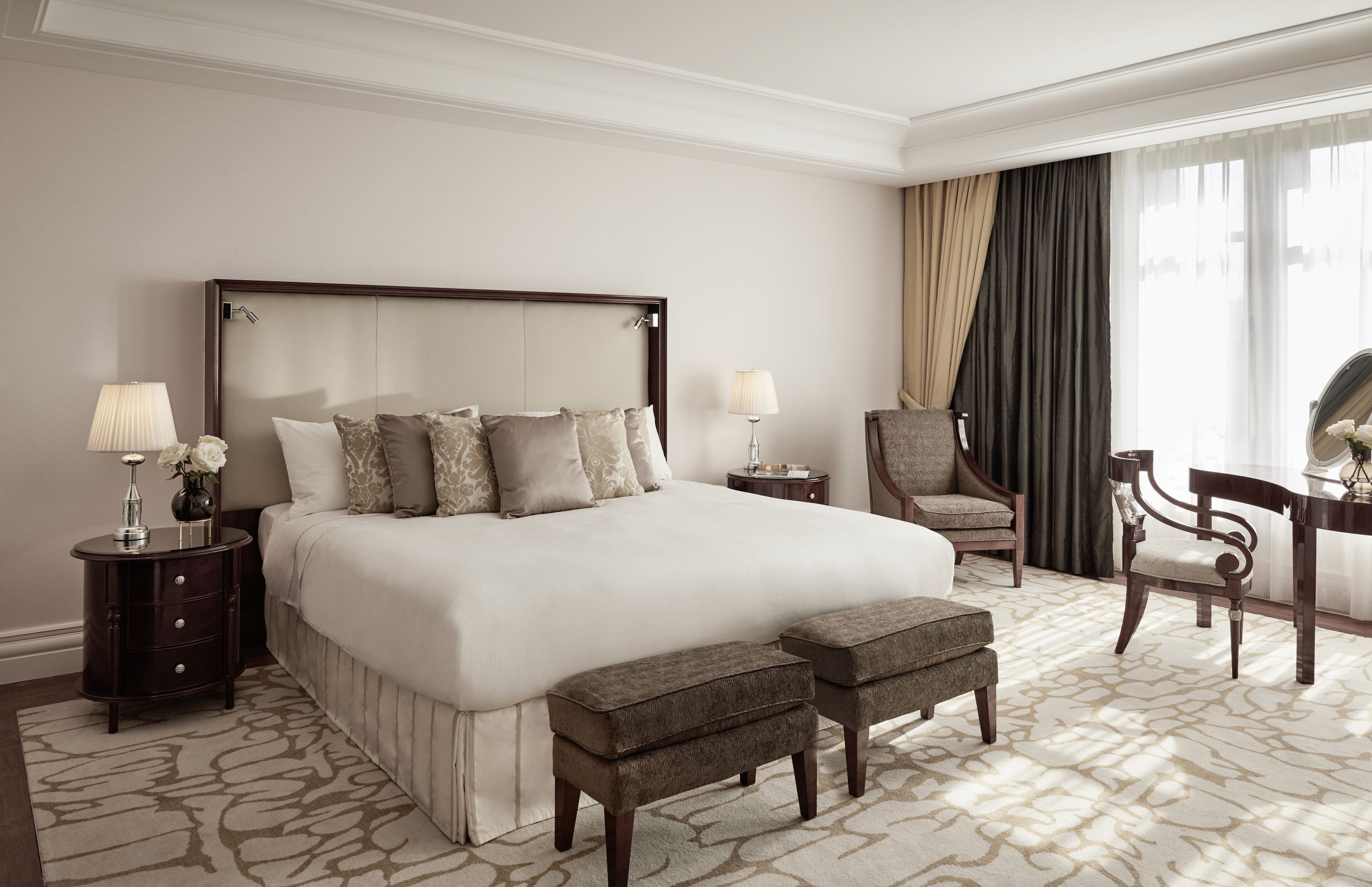 A spacious hotel room with a large bed, two bedside tables, a chair, a desk, and a large window with curtains.
