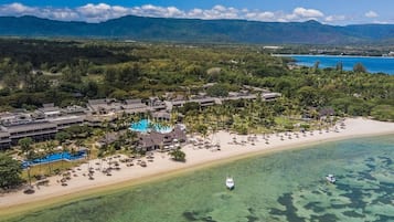 Vue aérienne d’un complexe hôtelier doté d’une piscine, d’une plage et d’eaux cristallines.