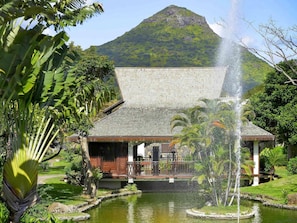 A building with a water fountain, surrounded by greenery and a mountain in the background.