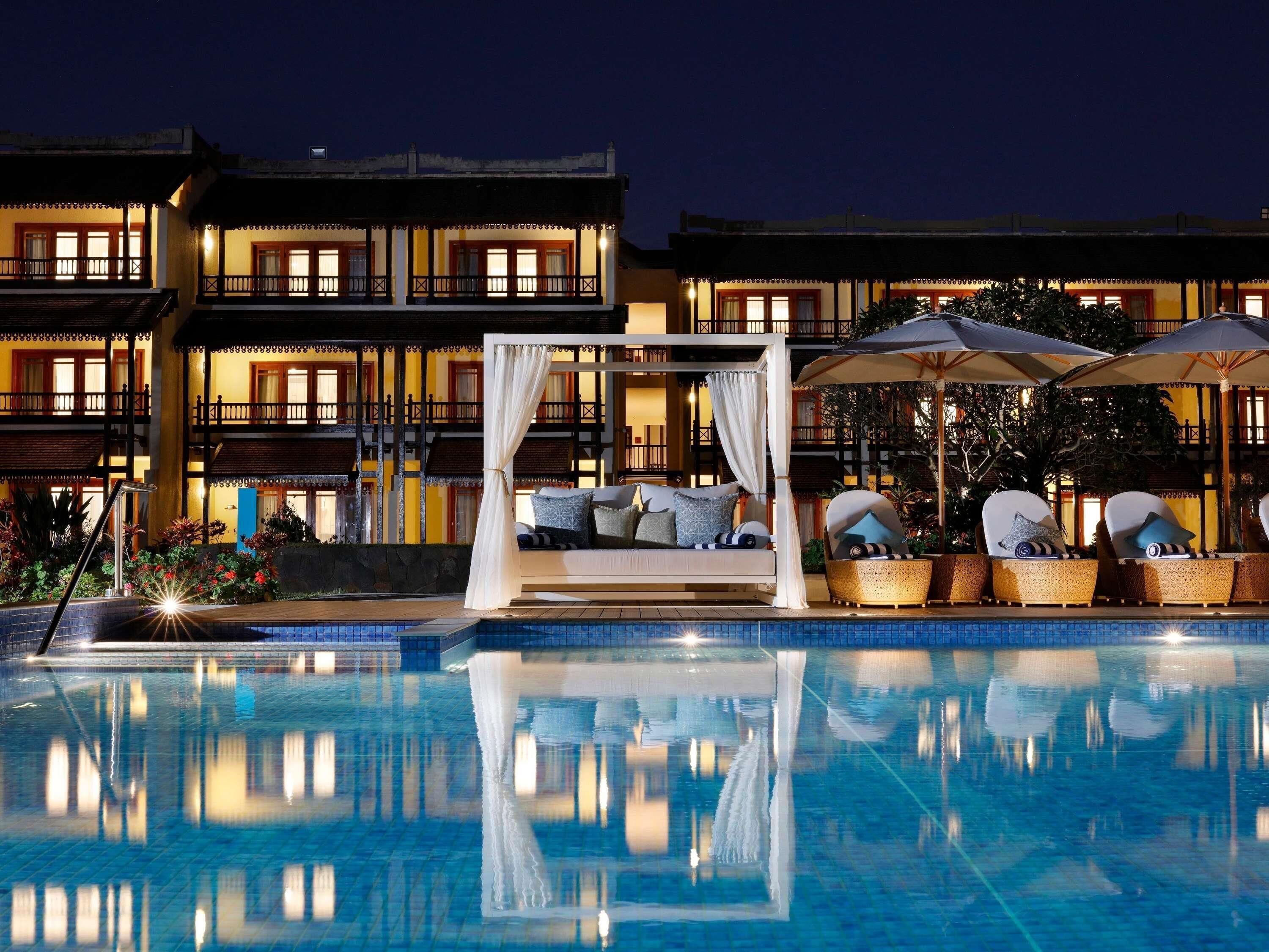 Zona junto a la piscina con una cama, sillones de descanso y sombrillas.