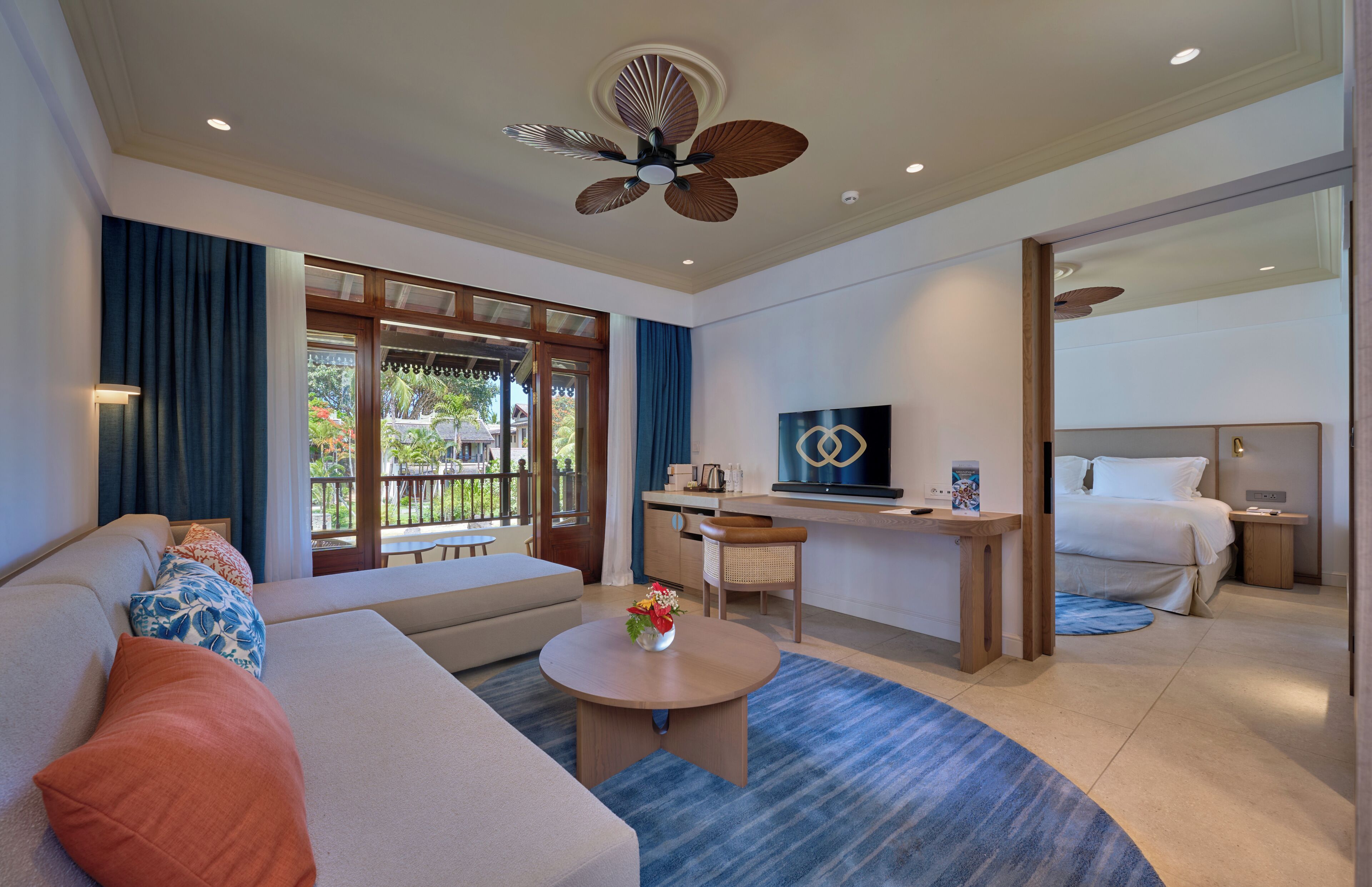 A modern hotel room with a sofa, a desk, a television, a bed, and a balcony with a view of greenery.
