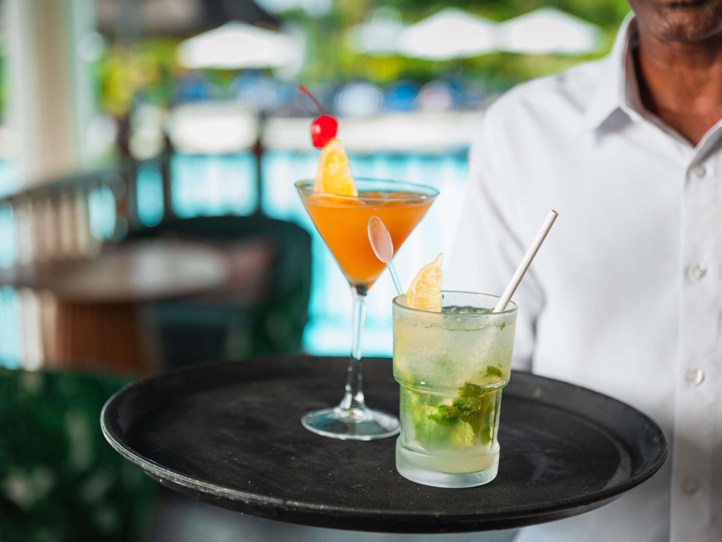 A tray with two drinks, one in a martini glass and one in a highball glass, both with garnishes.