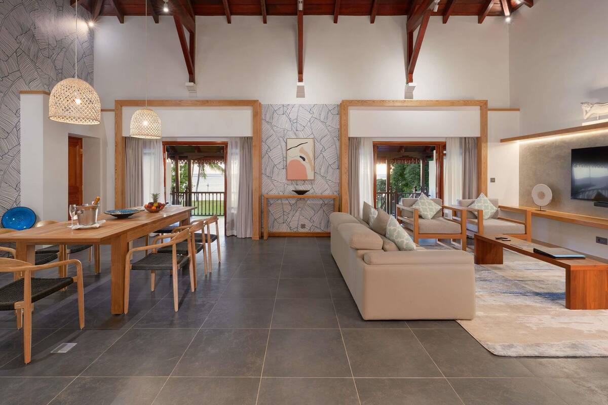 A spacious living area with a sofa, dining table, and chairs, a TV, and a balcony with a view.