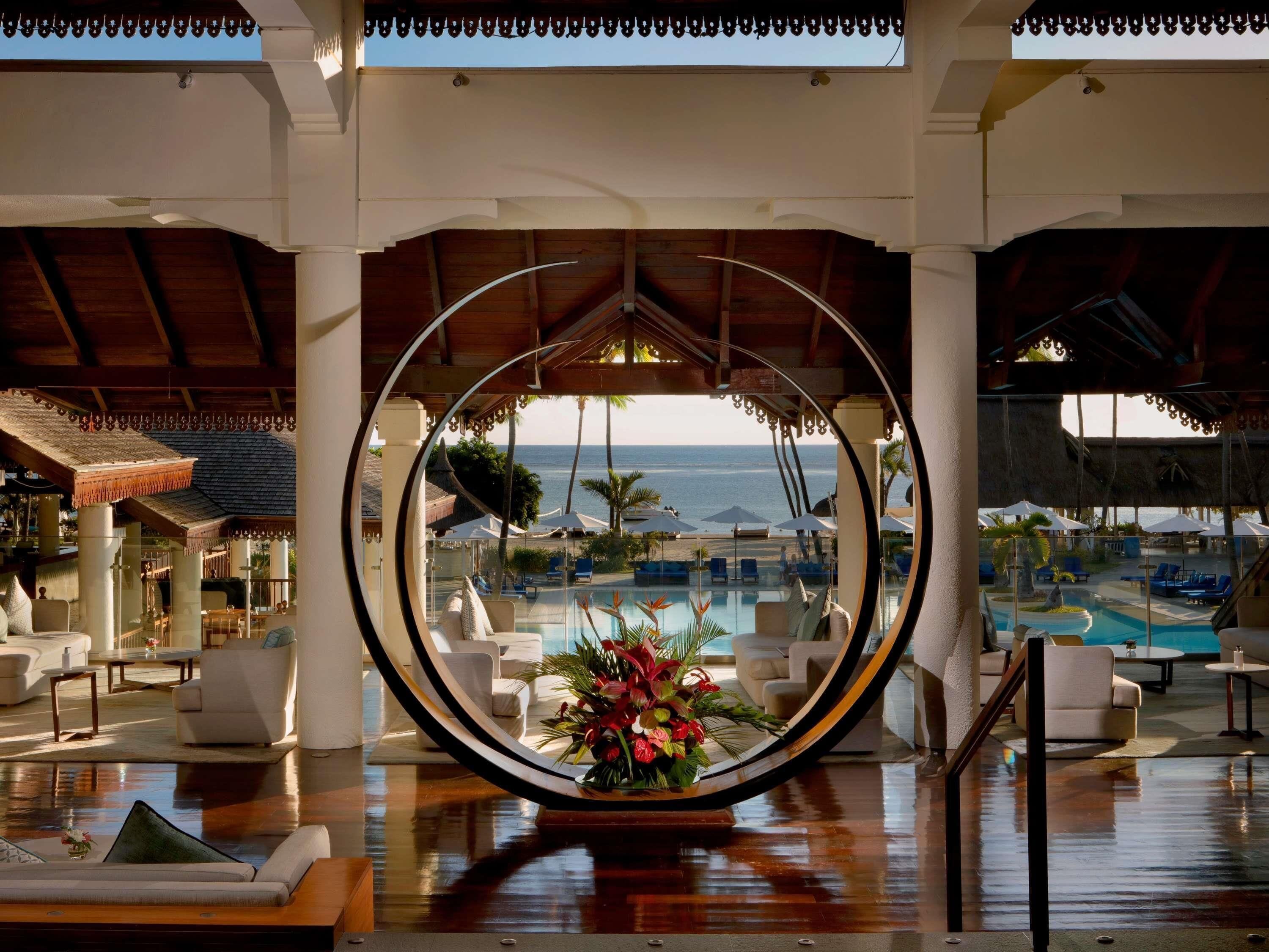 A lounge area with a view of the pool and beach, featuring a circular mirror, comfortable seating, and a floral centerpiece.