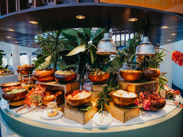 A buffet setup with various food items in wooden bowls, surrounded by plants and decorative elements. - Sofitel Mauritius L'Imperial Resort & Spa (Flic-en-Flac)
