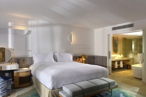A modern hotel room with a large bed, bedside tables, a bedside lamp, a small seating area, and a bathroom with a bathtub and sink.
