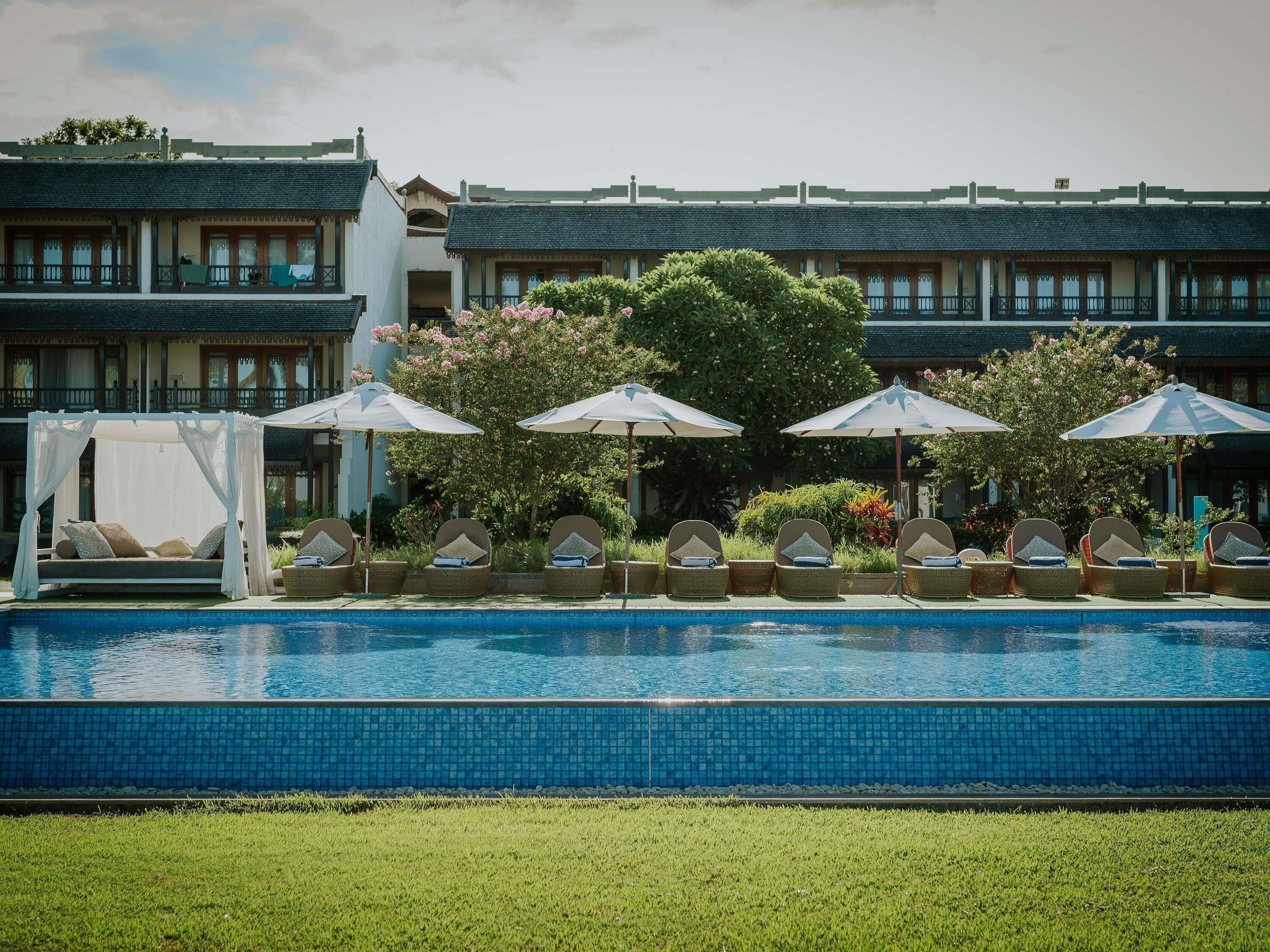 Una piscina con sillas de descanso y sombrillas, rodeada por un edificio con techo de tejas.
