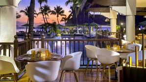 A restaurant with a view of a pool and palm trees, featuring white chairs and a wooden table. - Sofitel Mauritius L'Imperial Resort & Spa (Flic-en-Flac)