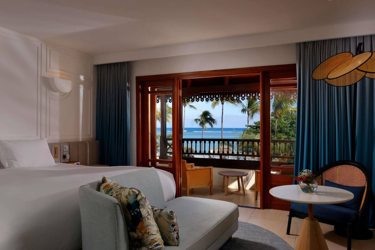 A hotel room with a bed, a sofa, a small table, and a view of the ocean.