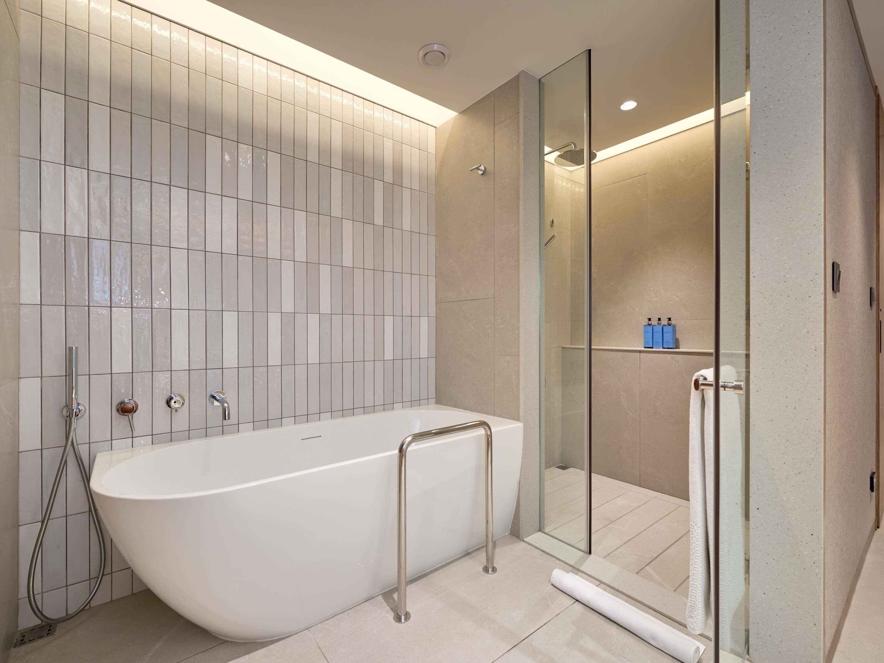 A modern bathroom with a freestanding bathtub, a glass-enclosed shower, and a tiled wall.