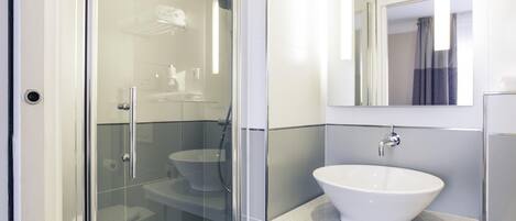 A modern bathroom with a glass shower enclosure, a white sink, and a mirror above it.