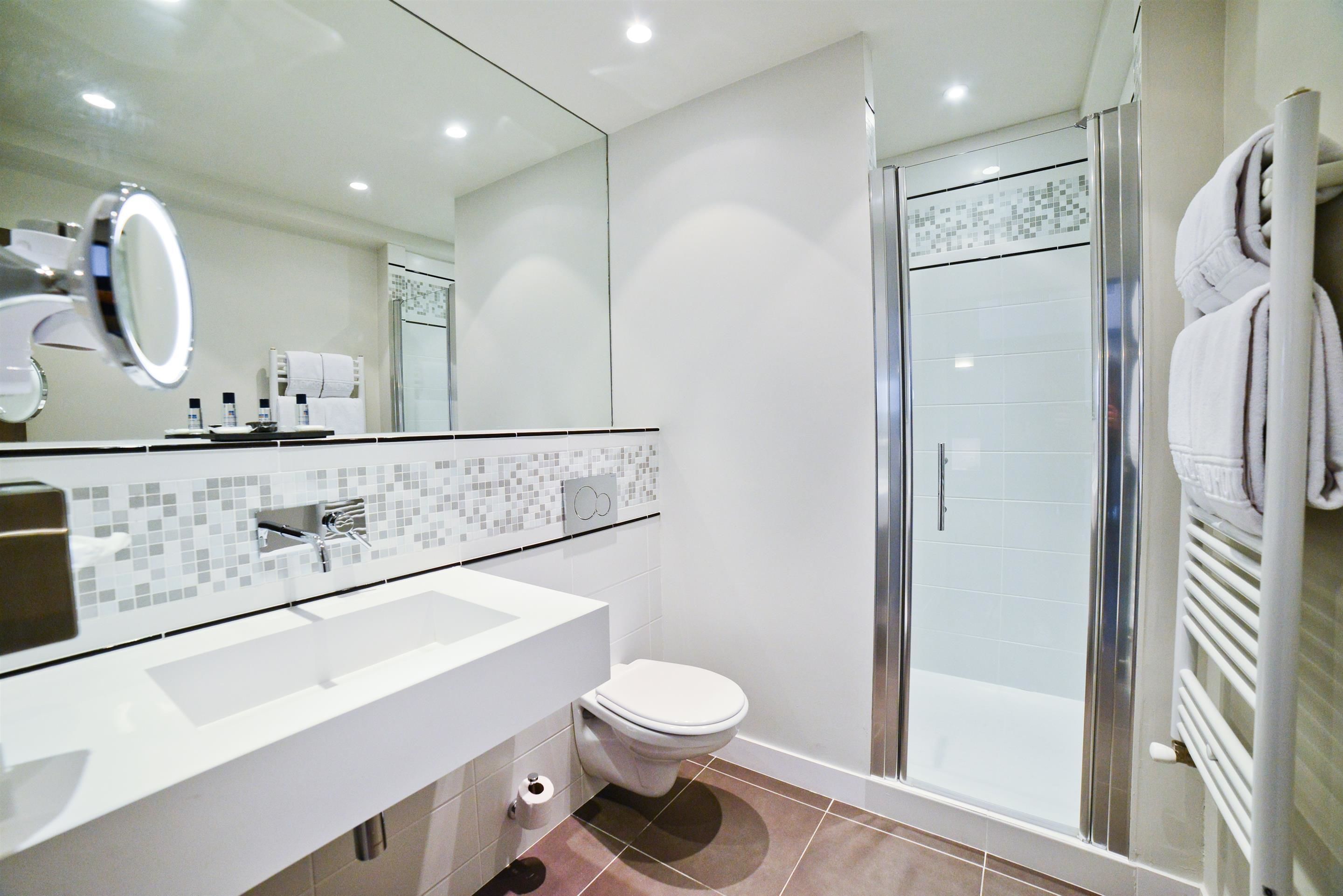 Un baño moderno con lavamanos blanco, inodoro y ducha con mampara de vidrio.