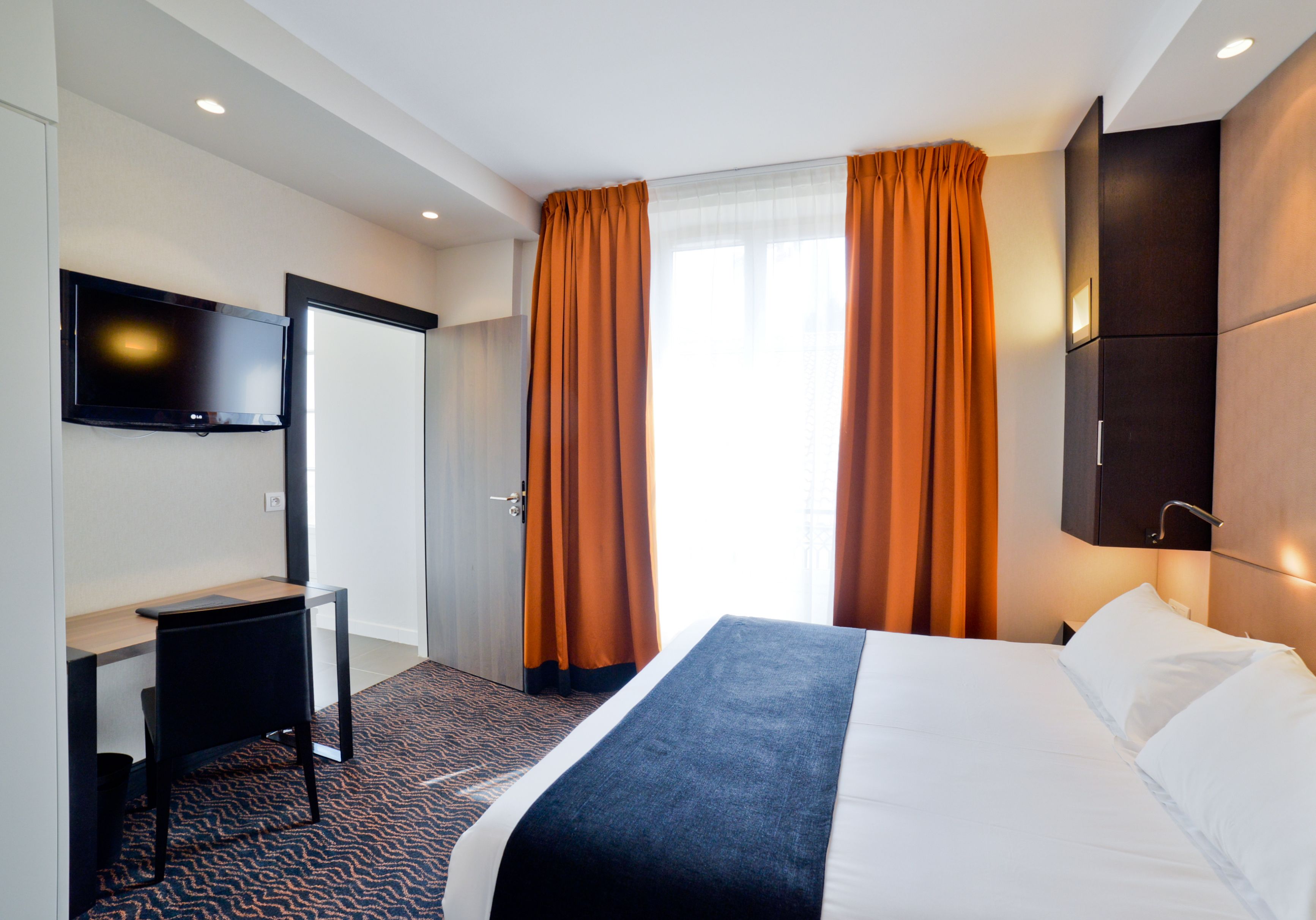 A hotel room with a bed, a desk, a television, and a wardrobe.