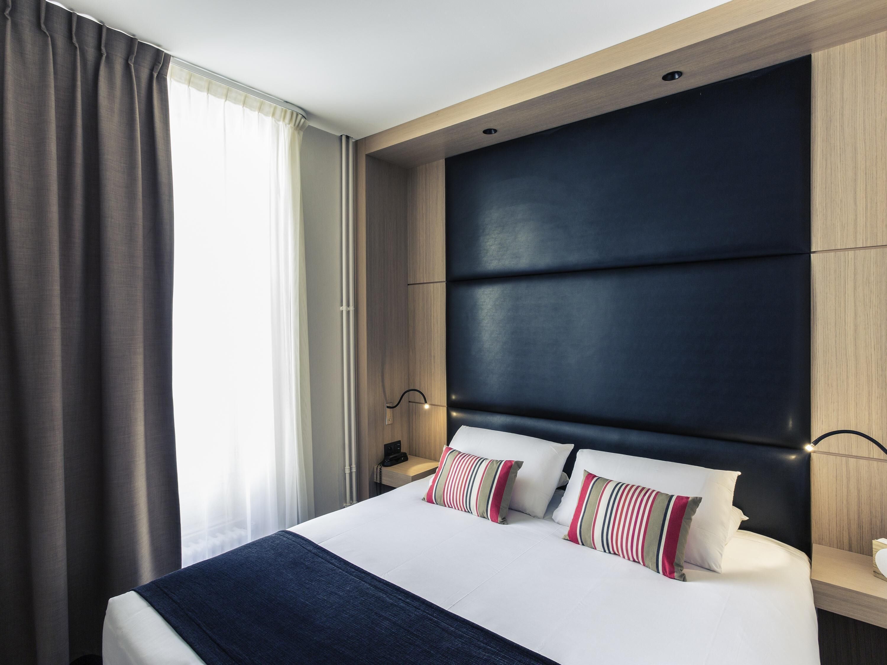 Habitación de hotel moderna con una cama grande, un cabecero oscuro y una mesita de noche con lámpara.