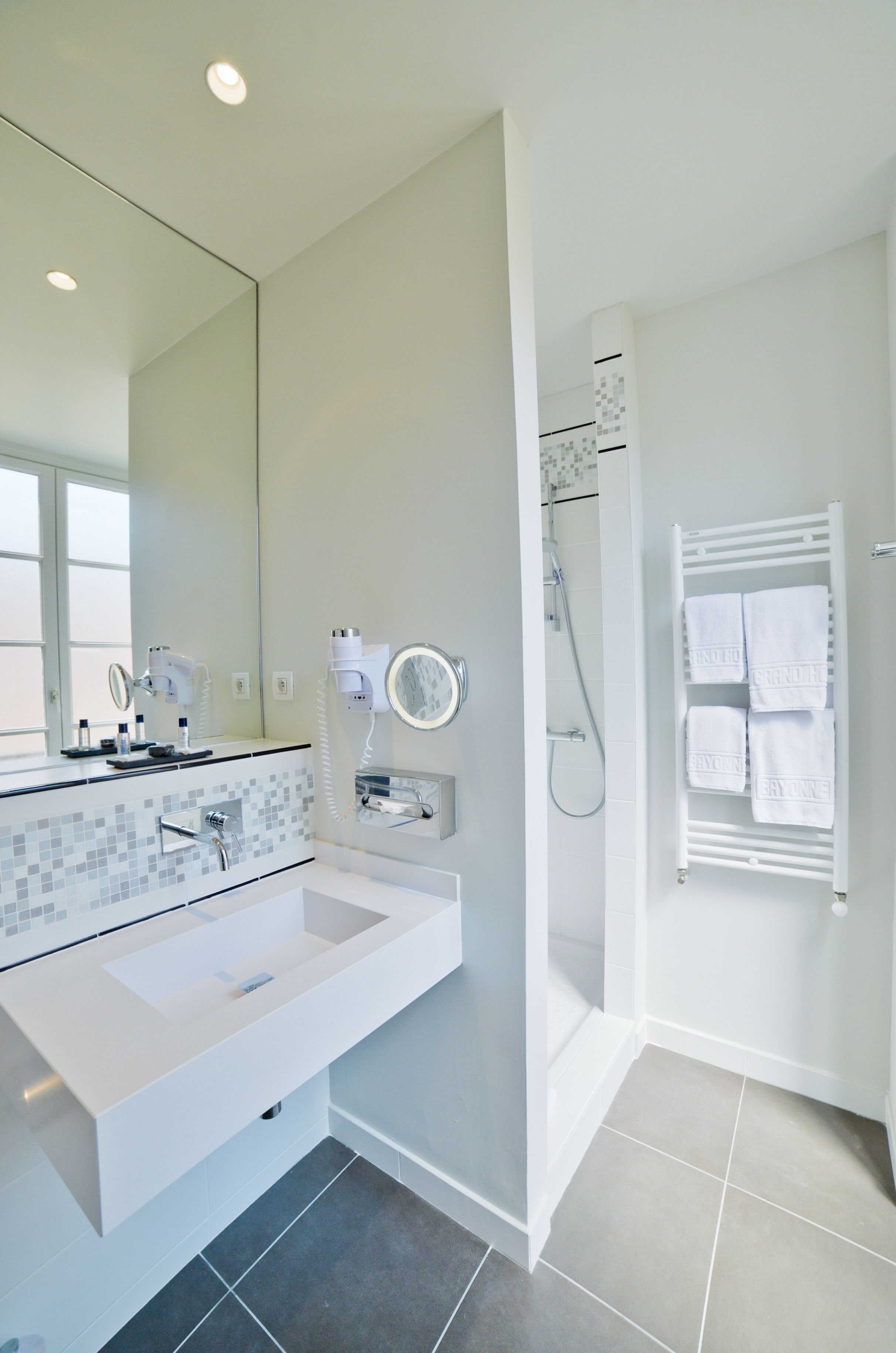 Une salle de bain moderne avec un grand miroir, un lavabo blanc, un sèche-cheveux et un porte-serviettes.