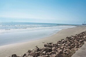 A beach with a rocky shoreline and a pier in the distance. - Wingate by Wyndham Galveston Beachfront at the Seawall (Galveston)