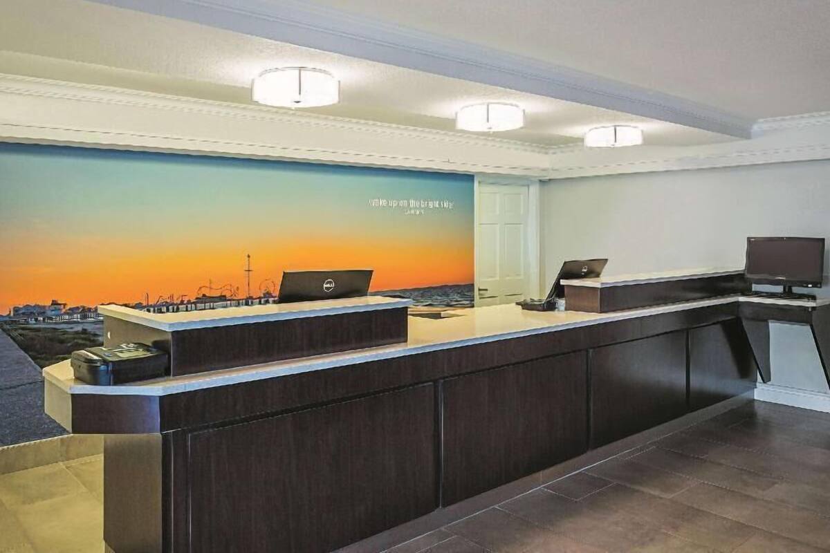 A reception desk with two computers, a wall mural, and a door to the right.
