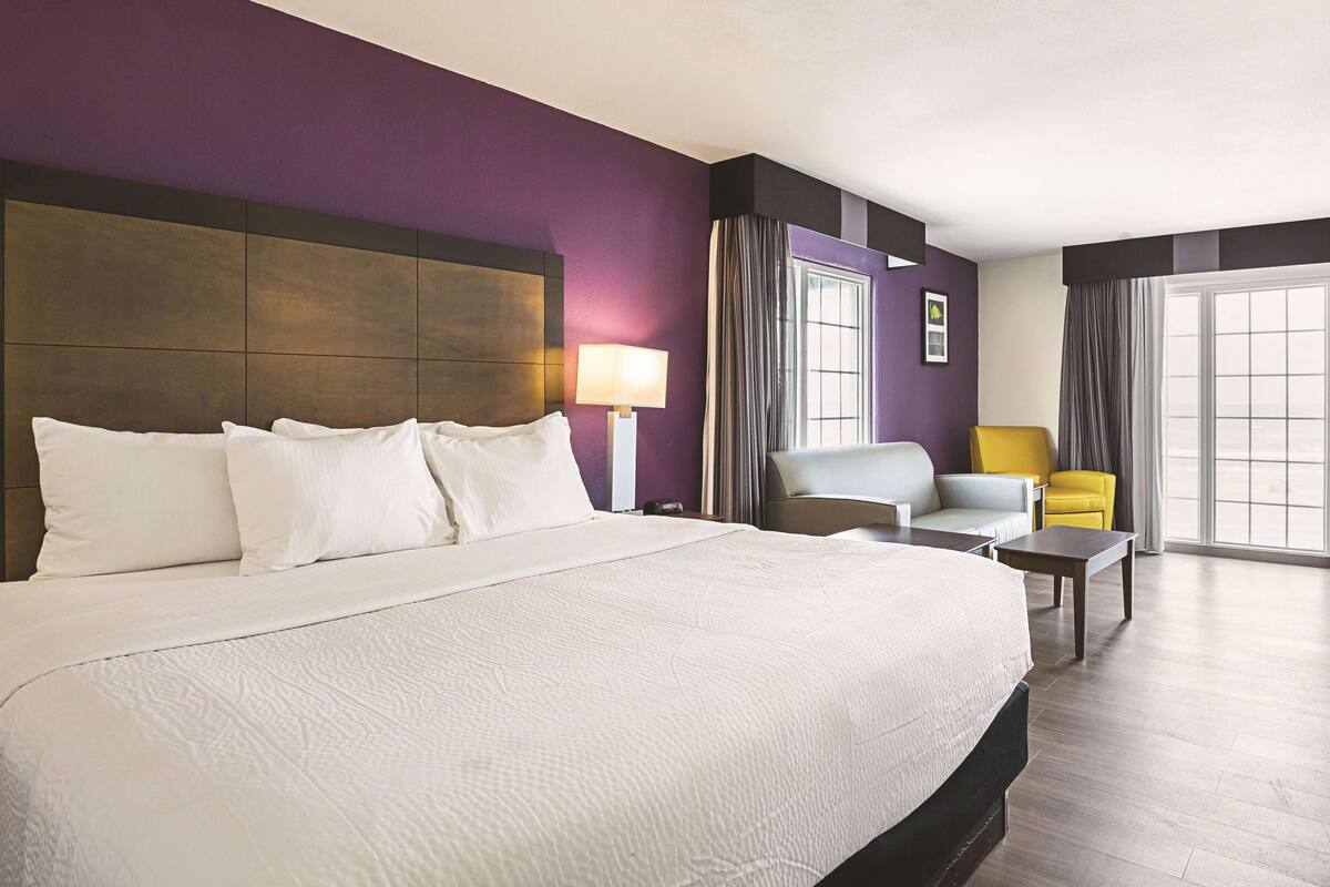 A hotel room with a large bed, a desk, two chairs, and a window with curtains.