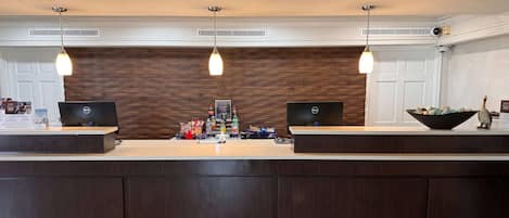 Ein Empfangsbereich mit einer Holzwand, zwei Computertischen und einer zentralen Rezeption mit verschiedenen Artikeln.