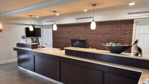 A reception desk with a flat-screen TV, two pendant lights, a wooden accent wall, and a decorative bowl with items. - Wingate by Wyndham Galveston Beachfront at the Seawall (Galveston)
