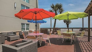 An outdoor patio with wicker furniture, a round table, and colorful umbrellas. - Wingate by Wyndham Galveston Beachfront at the Seawall (Galveston)