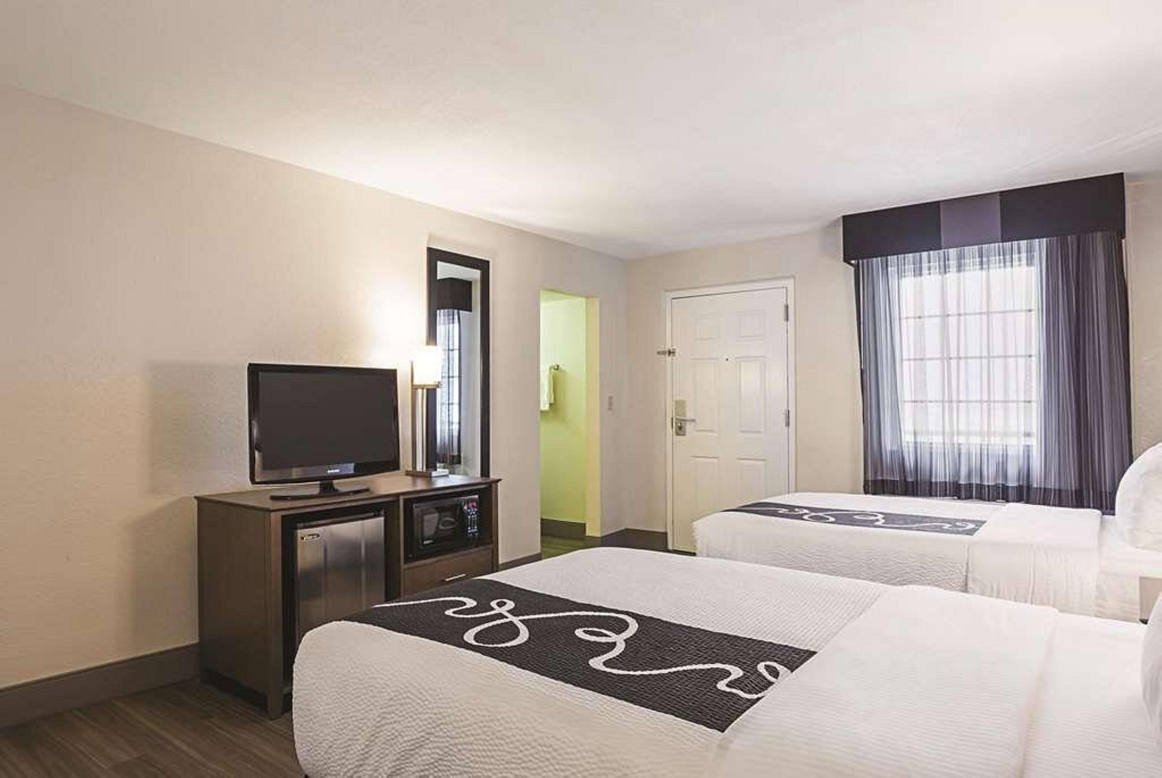 Een hotelkamer met twee bedden, een televisie, een bureau en een deur.