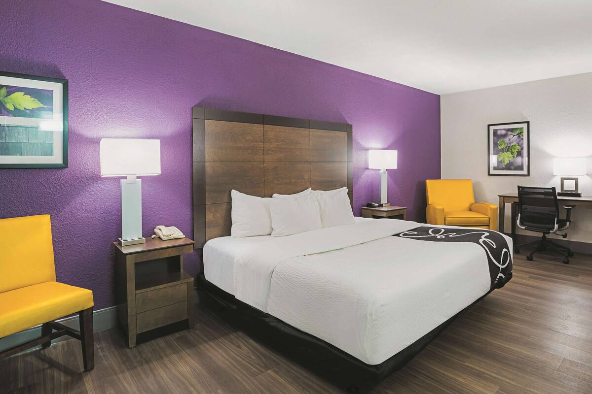 A hotel room with a large bed, two bedside tables with lamps, a desk with a chair, and a small chair.
