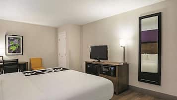 Ein Hotelzimmer mit Bett, Fernseher, Schreibtisch, Stuhl und Spiegel.
